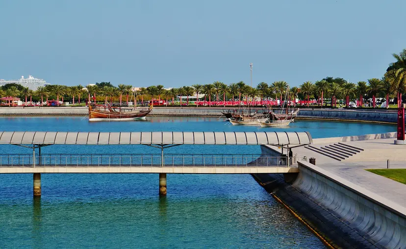 A footbridge over the water at MIA Park in Doha, with dhows moored beyond