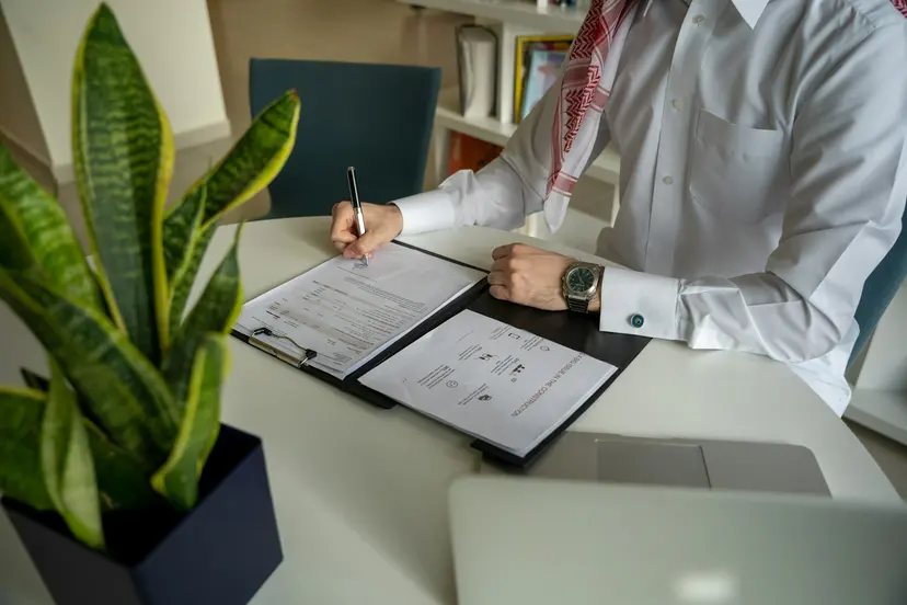 A man in a ghutra writing notes in a folder at an office desk in Doha