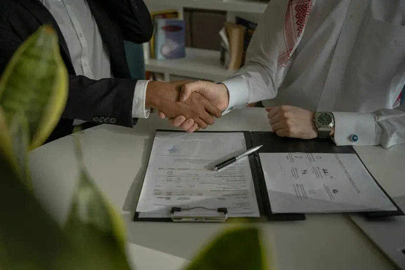 Two men shaking hands over signed company papers on a clipboard