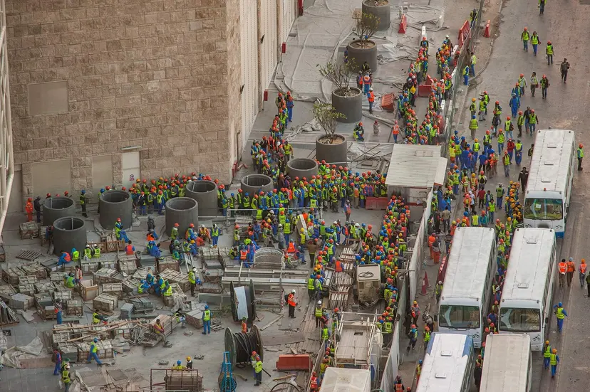 Construction workers in safety vests queuing for buses beside a building site in West Bay, Doha