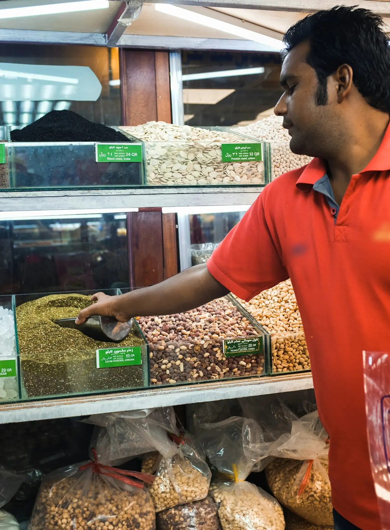 A shop worker in Doha scooping nuts beside labelled product bins