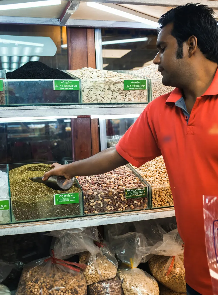 A shop worker in Doha scooping nuts beside labelled product bins
