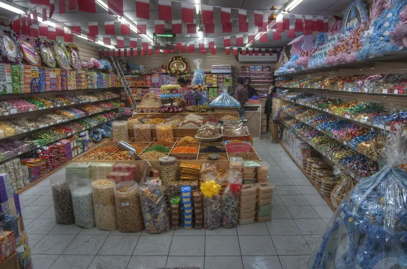 Shelves of sweets, nuts and gift boxes under Qatar flag bunting in a Souq Waqif shop