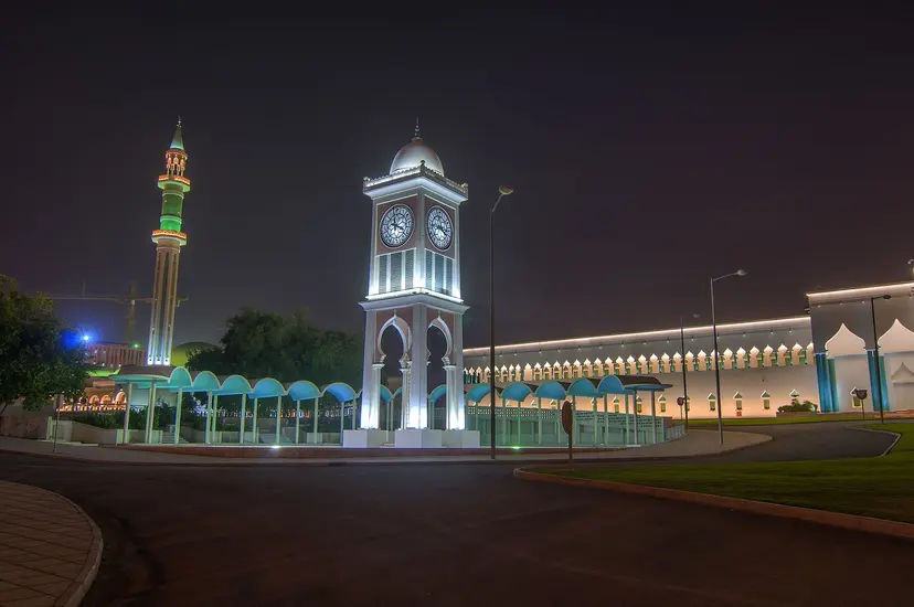 The clock tower in front of the Amiri Diwan in Doha, lit at night, with a minaret behind