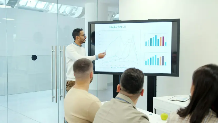 An adviser presenting sales charts on a large screen to three colleagues