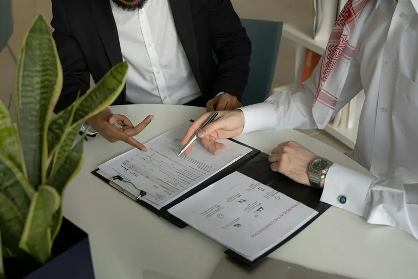 Two businessmen reviewing and signing company papers at a table