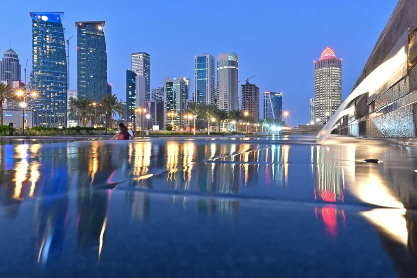 Doha towers lit at dusk, reflected on a wet promenade