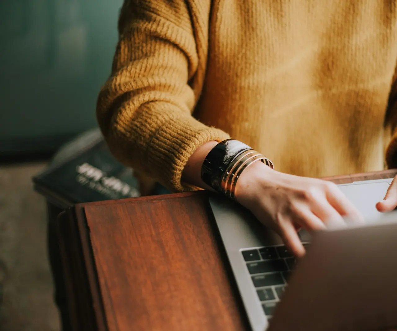 A person typing on a laptop at a wooden desk at home