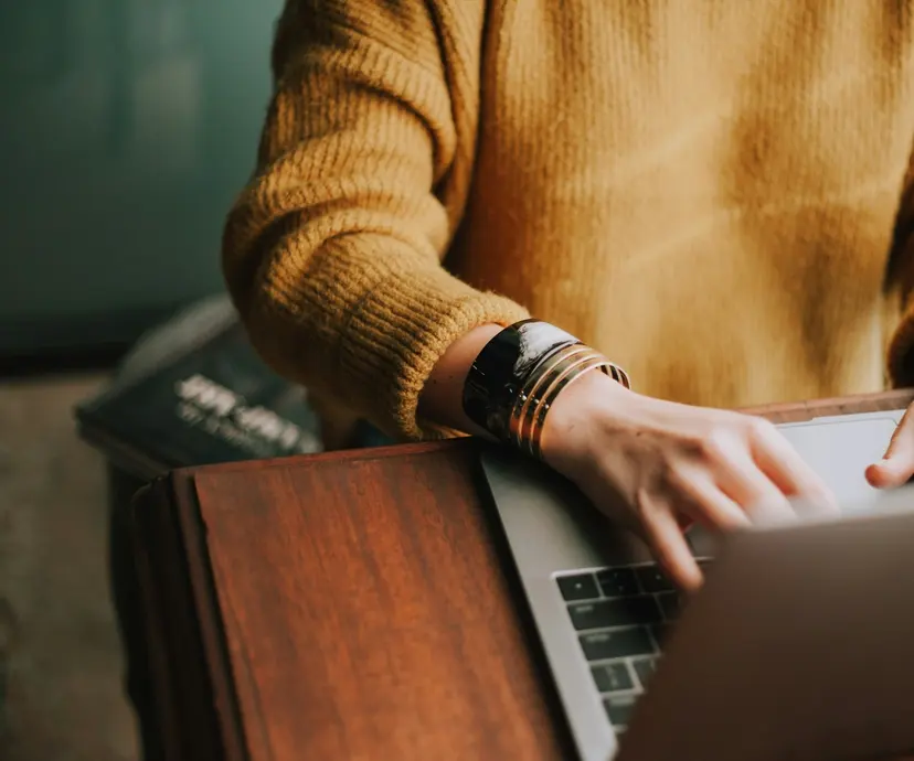 A person typing on a laptop at a wooden desk at home