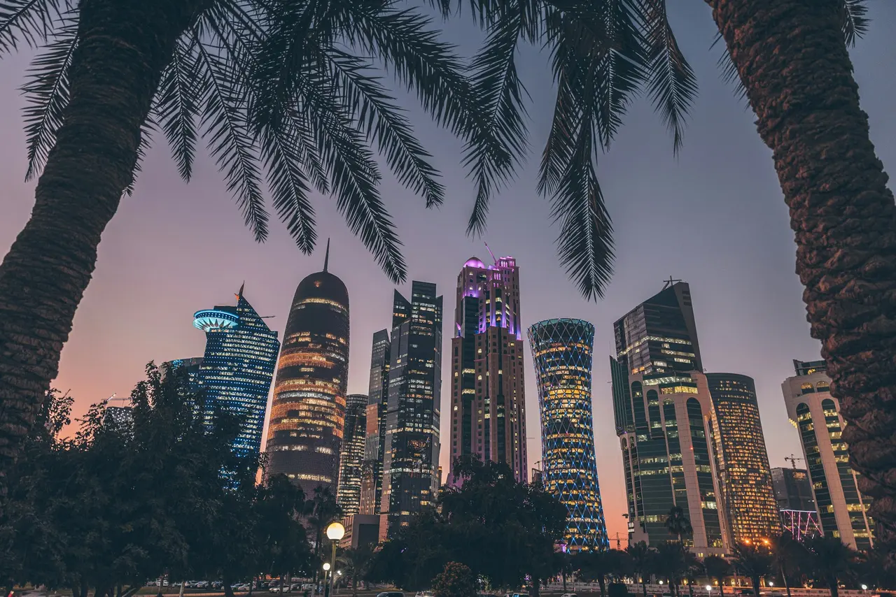 West Bay towers in Doha lit at dusk, framed by palm leaves