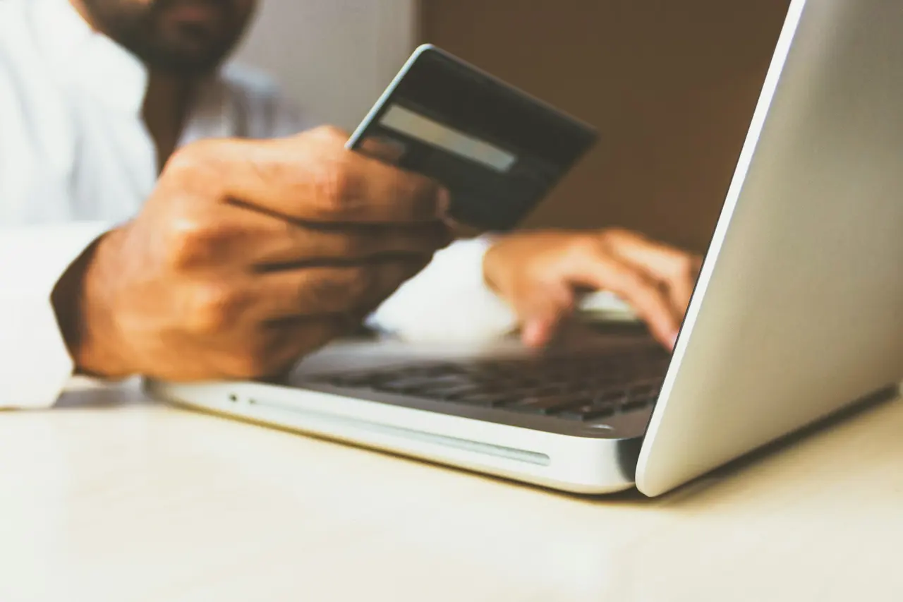 A man holding a bank card beside an open laptop