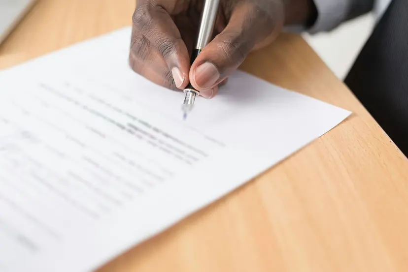 A hand signing a printed contract with a fountain pen