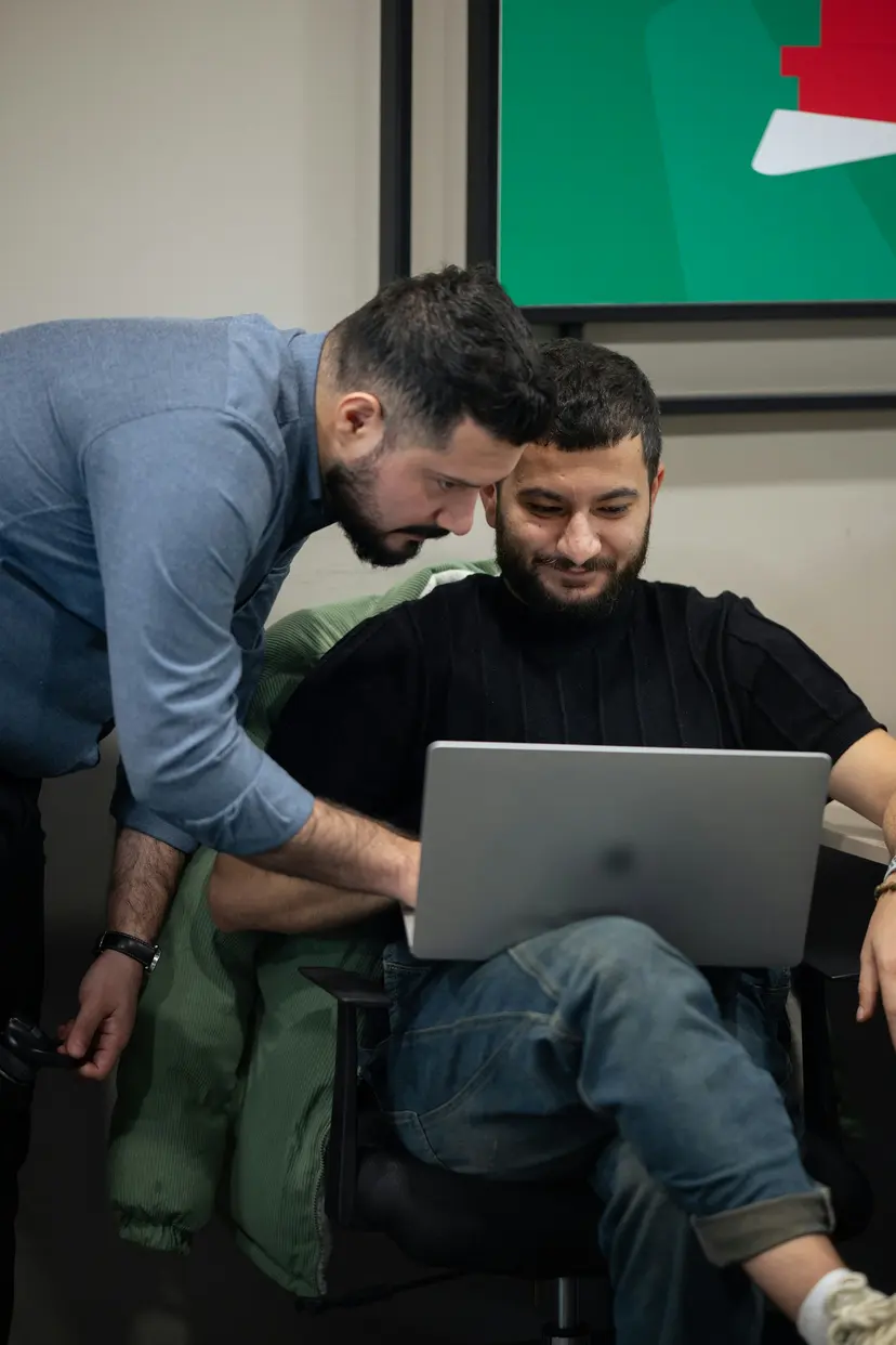 An adviser leaning over a colleague’s laptop to go through a plan with him