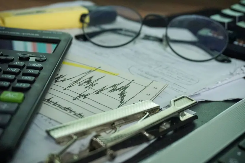 Printed line charts on a clipboard beside a calculator and glasses