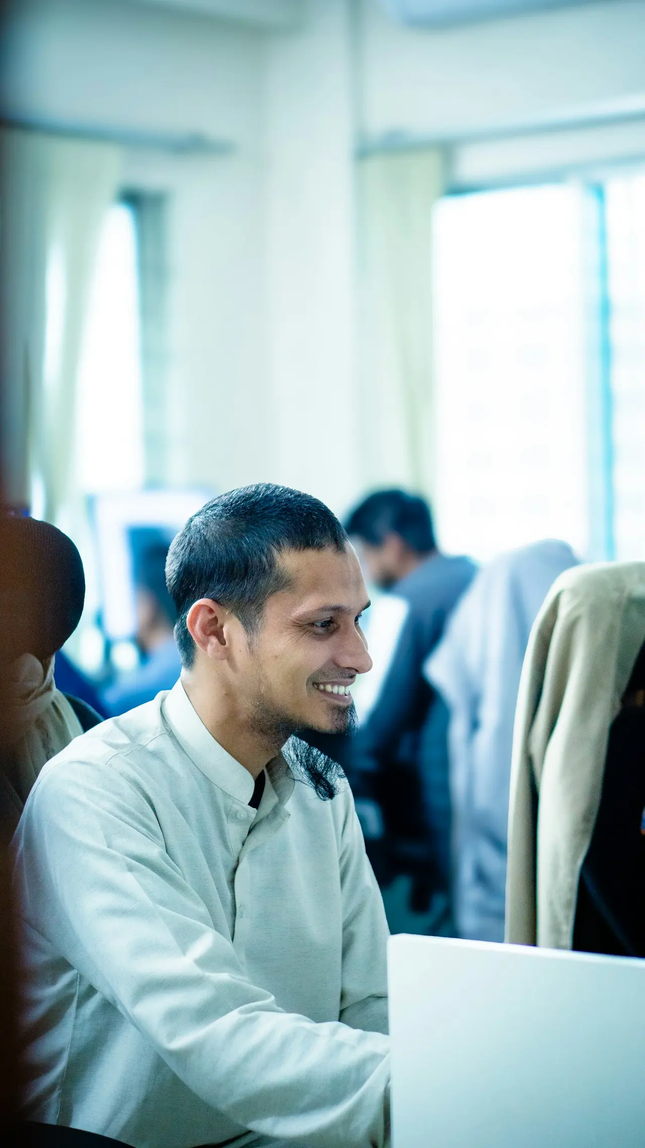 An employee smiling at his laptop in a busy open-plan office
