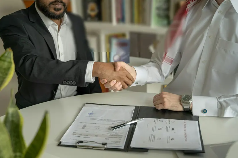 Two businessmen shaking hands across a desk with documents