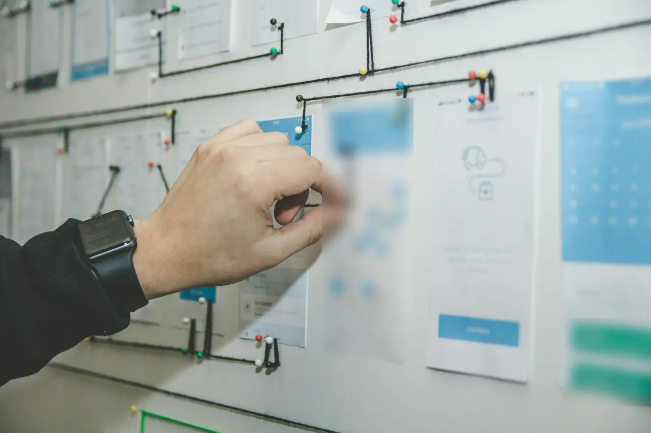 A hand pinning the steps of a work process on a planning board