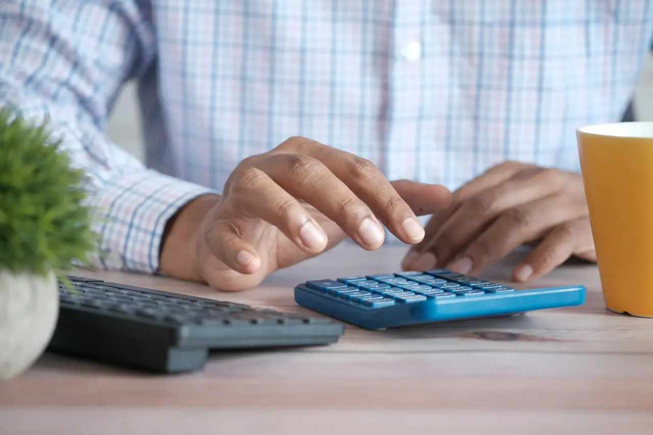 Hands working on a calculator beside a keyboard